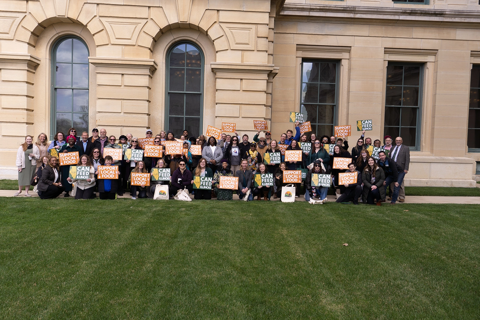 A group of food and farm advocates pose with their protest signs in front of a legislative building.